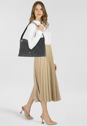 Graue Wildlederhandtasche mit strukturiertem Design, silberner Hardware und langem Riemen, gehalten von einer Person in weißem Hemd und beigefarbenem plissiertem Rock.