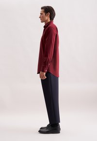 Bordeaux overhemd met lange mouwen, gecombineerd met marineblauwe broek en zwarte schoenen. Glad textuur, op maat gemaakte pasvorm en zichtbare details van het shirt.