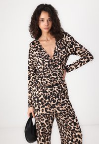 Mono de leopardo en beige y negro, con un profundo escote en V, mangas largas y cintura elástica. La modelo sostiene un bolso negro.