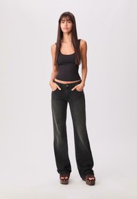 Schwarzes Tanktop mit weit geschnittenen, verwaschenen schwarzen Jeans. Das Outfit hat eine hohe Taille und zwei vordere Taschen, kombiniert mit Plateausandalen.