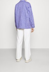 Světle fialová košile s dlouhým rukávem a bílým vlnkovým vzorem, volný střih, v kombinaci s bílými širokými kalhotami a masivními krémovými teniskami.