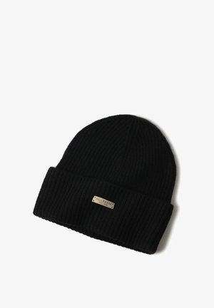 Mann mit leichtem Bart, der eine schwarze, gerippte Strickmütze mit der Aufschrift "Bellemere New York" und einen schwarzen Pullover mit Rundhalsausschnitt trägt.