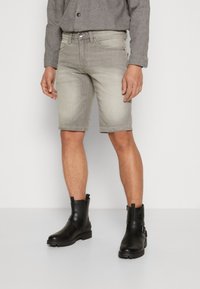 Shorts in denim grigio chiaro con una vestibilità slim e orlo arrotolato, abbinati a stivali alla caviglia in pelle nera con dettagli in fibbia.