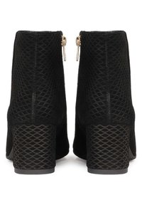 Bottes noires à chevilles avec une superposition en maille texturée, des fermetures éclair métalliques à l'arrière et un talon épais à motif. Doublure intérieure lisse.