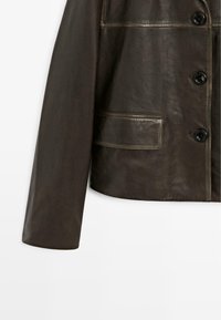 Manica in pelle marrone scuro con tre bottoni neri e una tasca rettangolare su uno sfondo bianco.