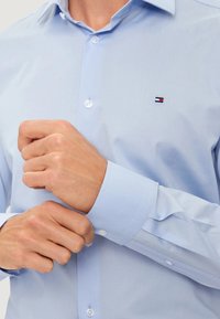 Camicia da uomo azzurro chiaro in tessuto liscio con colletto appuntito, polsini abbottonati e piccolo logo ricamato sul petto.