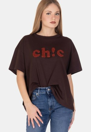 T-shirt oversize marrone con lettering rosso "ch!c" testurizzato sul davanti. Materiale in cotone morbido, vestibilità rilassata, maniche corte e scollatura rotonda.