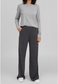 Grauer Langarmoberteil und locker sitzende, dunkelgraue Hose aus weichem Stoff, kombiniert mit weißen Turnschuhen, vor neutralem Hintergrund.