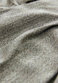 Textilie s herringbone vzorem v šedých a černých odstínech, která má měkký, strukturovaný povrch přirozeně vlnící se.
