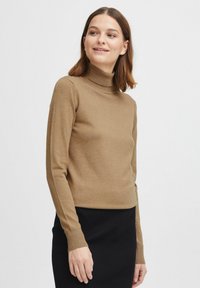 Maglione collo alto marrone in materiale a maglia fine, design aderente con maniche lunghe e polsini a costine, abbinato a una gonna nera a costine.