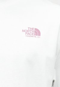 Λευκό φούτερ με στρογγυλή λαιμόκοψη που φέρει ροζ λογότυπο της The North Face και το κείμενο «Yosemite, CA» στην αριστερή πλευρά του στήθους.