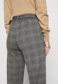 Pantaloni a scacchi grigi con una vestibilità rilassata, dotati di cintura e pieghe sottili. La texture del materiale appare liscia con un design strutturato.