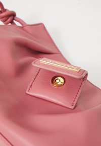 Pink leather handbag with a smooth texture, featuring a gold-tone hardware tag that reads "LOVE MOSCHINO" and a snap closure detail.
