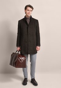 Dark wool overcoat with a high collar, two buttons, gray trousers, brown leather bag with unique flap, and black shoes. Neutral background.
