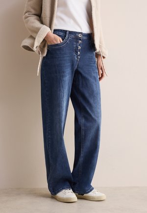 Wijde jeans in donkerblauw met een vijfknopen sluiting, voorzakken en een relaxte pasvorm, gecombineerd met witte sneakers.