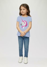 Lichtblauwe t-shirt met een eenhoornontwerp versierd met pailletten in roze en zilver; gecombineerd met blauwe jeans en witte sneakers.