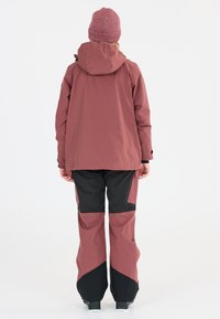 Vattentät skidjacka i rosarosa med huva, kombinerad med svarta skidbyxor med rosa detaljer och en avslappnad passform, lämplig för kallt väder.