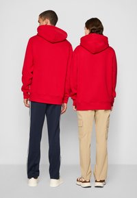 Røde hettegensere med store hetta, avslappet passform, båret med marineblå og beige bukser. Hettegenserne har ribbestrikkede mansjetter og nederkant.