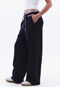 Pantaloni navy a gamba larga realizzati in tessuto morbido, con una cintura a righe dotata di cordino, tasche laterali e una vestibilità rilassata.