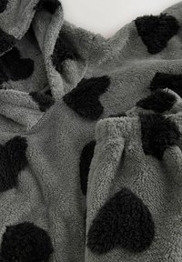 Harmaa fleeceloimi, jossa on mustia sydämenmuotoisia kuvioita, pehmeä, teksturoitu pinta ja miellyttävän pehmeä tuntuma.