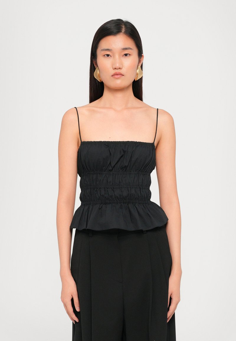 Black peplum top with thin straps, gathered bodice, and a ruffled hem. Smooth fabric with subtle sheen, paired with high-waisted black pants.