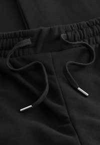 Svarta sweatpants med resårmidja och justerbara dragsnören med metallspetsar, tillverkade av mjukt bomullstyg.