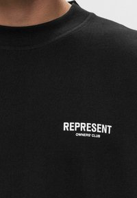 Sudadera de algodón negro con cuello redondo, que presenta el texto bordado en blanco "REPRESENT OWNERS' CLUB" en el pecho. Textura suave.