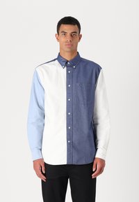 Chemise à boutons avec un design en blocs de couleur comprenant des sections bleu foncé, bleu clair et blanc. Fabriquée en coton, elle dispose d'un col classique et d'une poche.