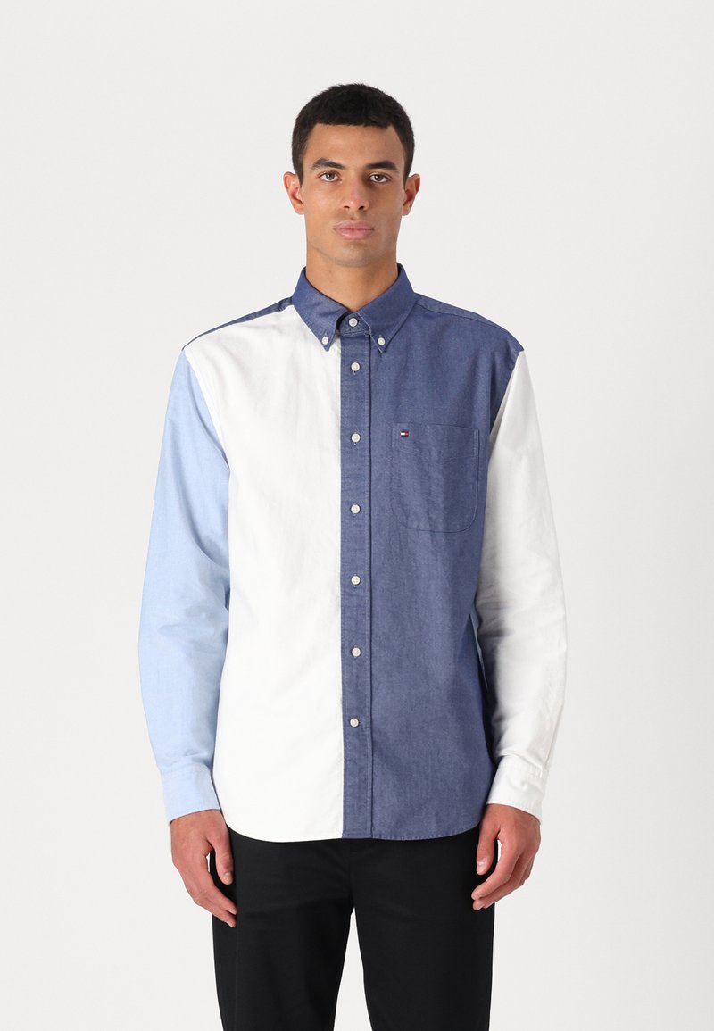 Chemise à boutons avec un design en blocs de couleur comprenant des sections bleu foncé, bleu clair et blanc. Fabriquée en coton, elle dispose d'un col classique et d'une poche.