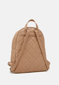 Quilted beige backpack with dual top handles and adjustable shoulder straps. Made of smooth fabric, featuring diamond-patterned texture.