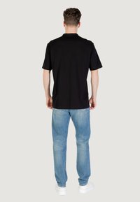 Camiseta negra de manga corta, material de algodón, corte relajado, cuello redondo, combinada con vaqueros de mezclilla azul claros y zapatillas blancas.