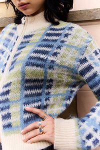Cardigan tricotat, prezentând un amestec de nuanțe de albastru, verde și crem, cu un model în carouri. Guler înalt și închidere cu fermoar, textură moale.