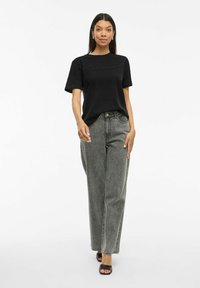 Svart bomullströja med präglad text "balance", ihopparad med grå randiga vida jeans och svarta öppna klackskor.