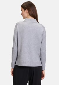 Grauer Strickpullover mit hohem Kragen, geripptem Saum und strukturierten Ärmeldetails. Weiches Material und lässige Passform.