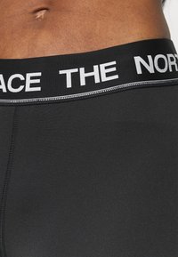 Shorts de sport noirs avec une large taille élastique arborant un texte blanc, texture lisse et coutures plates pour un confort accru.
