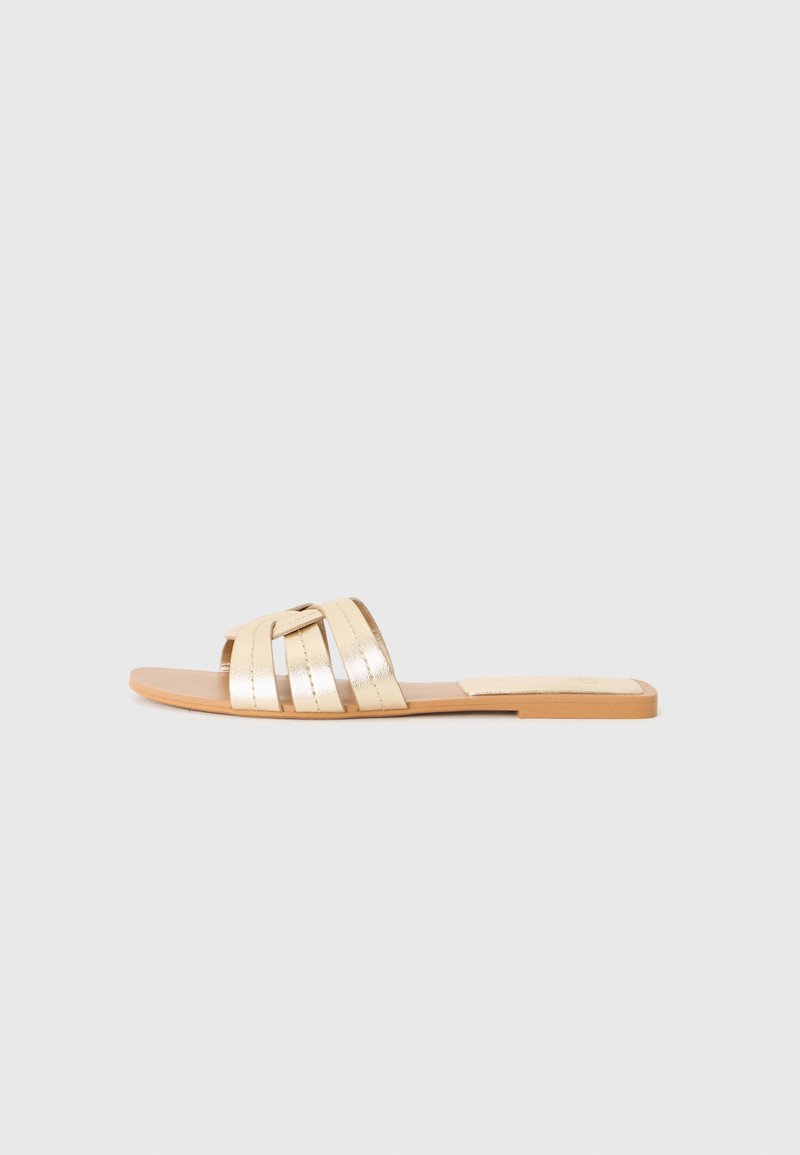 Sandalia deslizante metálica dorada con múltiples correas superpuestas, suela plana y una plantilla suave beige. Diseño sencillo para un fácil uso.