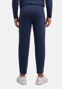 Marineblaue, gerippte Jogginghosen mit elastischem Bund, schmal zulaufenden Beinen und weißen Sneakers. Die Textur wirkt glatt, und die Passform ist locker.