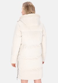 Vrouw in een lange, witte pufferjas met een grote capuchon, met de rug naar de camera, waarbij de achterkant en de ritsdetails aan de zijkant zichtbaar zijn.