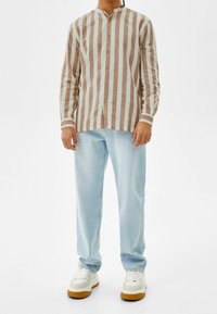 Randig långärmad skjorta i brun och ljusblå, med knapplist och bandkrage, matchad med ljusblå jeans och vita sneakers.