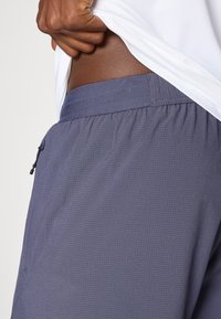 Tumedad hallid, kergest kangast lühikesed püksid, millel on tekstuuriga muster, elastne vöökoht ja küljes väike tõmblukuga tasku.