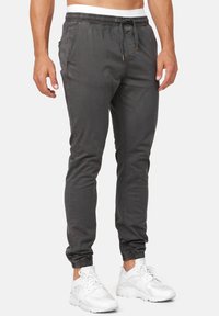 Pantalones de chándal grises con cintura elástica y puños. Con bolsillos laterales y un cordón con acentos en tono dorado. Se llevan con zapatillas blancas.