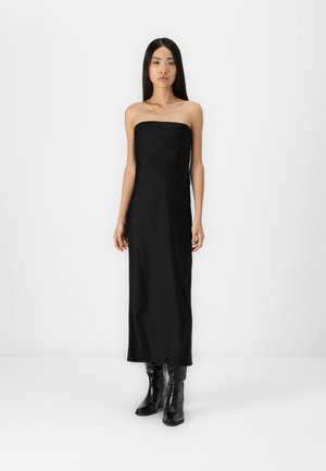 Svart strapless maxikjole laget av et glatt stoff med en tettsittende overdel og en rett silhuett, iført blanke svarte ankelstøvler.