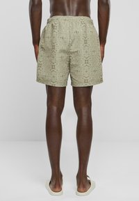 Herre badshorts med et mønster i dempet olivengrønn, elastisk midje og sidelommer. Teksturert stoff med avslappet passform.