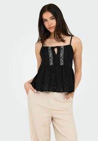 Czarny top peplum na cienkich ramiączkach, z dekoltem w kształcie kropli i białymi haftami w kwiaty wzdłuż Centrum. Teksturowany materiał z diagonalnymi wzorami w diamenty.