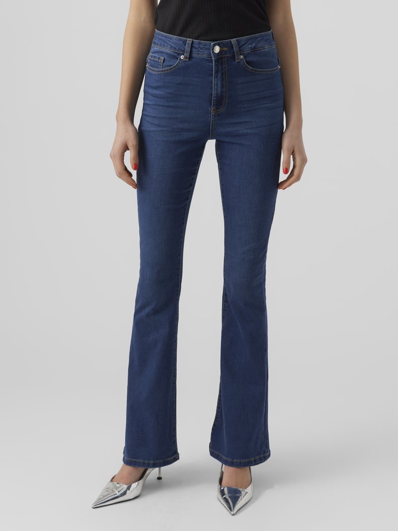 Sinine denimist laienevad teksad kõrgema taljega, viiega taskut ja puhta viimistlusega. Kanda metallik hõbedast kõrge kontsaga kingadega.