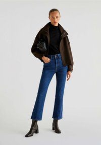Brown checked cropped jacket, black turtleneck, blue high-waisted jeans, black square-toed ankle boots, holding black bag.