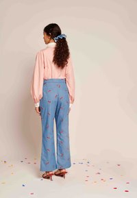 Svetlo roza bluza z napihnjenimi rokavi, v kombinaciji z modrimi hlačami z rdečimi češnjevimi potiski. Model nosi strapaste petke in modro gumico za lase.