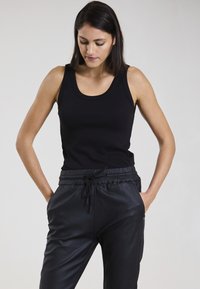 Schwarzes geripptes Tanktop mit breiten Schulterträgern, kombiniert mit schwarzen Jogginghosen mit Kordelzug, die eine glatte Textur und seitliche Taschen haben.