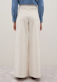 Pantaloni a gamba larga di colore crema realizzati in un tessuto testurizzato, con vita alta e doppie tasche posteriori, mostrati di spalle.