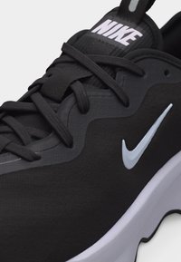 Μαύρο αθλητικό παπούτσι Nike με λευκό λογότυπο swoosh, μαύρα κορδόνια και λευκή μεσαία σόλα, με εμφανές τη γλώσσα που φέρει την ένδειξη "NIKE".